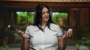 Barışçıl şehirde elinde makyaj fırçası ve sünger tutan bir kadın gösterişli güzellik odağı oluşturuyor..