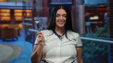 Üniformalı bir kadın lüks otel ortamında fırça tutuyor, rahat ve profesyonel bir konukseverlik havası var ve arka planda zarif bir dekor var..