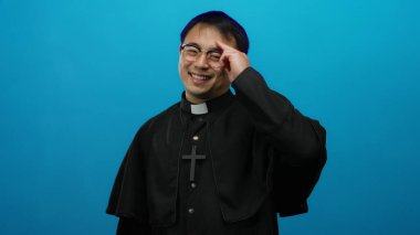 Mavi arka plana poz veren rahip kıyafeti giyen adam güven verici bir dini kavrama işaret ediyor. Jest ve ifade yoluyla güven ve inanca ilham veriyor..