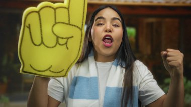 Canlı, enerjik bir atmosferde köpüklü parmaklarıyla tezahürat yapan kadın coşku ve neşe saçıyor..