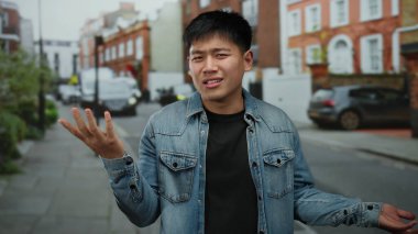 Etkileyici jestleri olan genç bir adam canlı bir şehir caddesinde duruyor, canlı şehir ortamını yakalıyor..