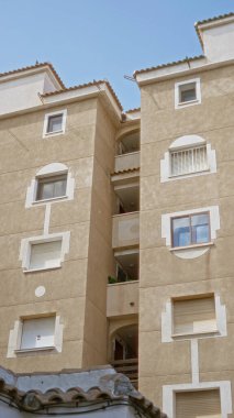 Güneşli İspanya 'da Akdeniz apartman cephesi bej kaplama duvarlar ve açık mavi gökyüzünün altında belirgin pencereler.
