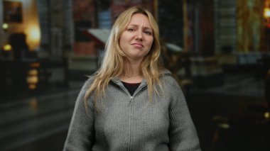 Kilise ortamında duygusal bir jest yapan, sarı saçlı, gri bir kazak giyen, mihrap geçmişi bulanık, kederli ya da kapalı alanlarda sıkıntı taşıyan bir kadın..