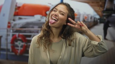 İspanyol kadın bir yolcu gemisinin güvertesinde canlı hayat halkaları ve okyanus zeminiyle barış işareti yapıyor. Genç enerjisiyle deniz kenarında neşeli bir anı yakalıyor..