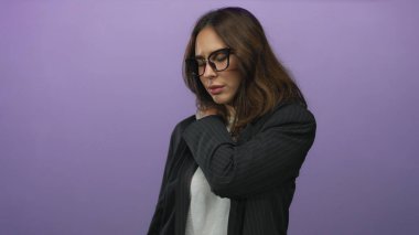 Gözlüklü genç İspanyol kadın beyaz gömlekli ceket giyiyor ve arka planda izole edilmiş mor bir arka plana karşı sırt ağrısı çekiyor..