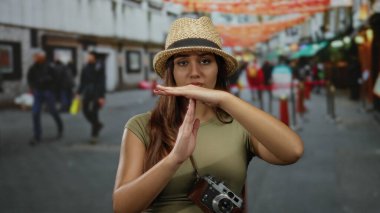 İşlek bir sokak sahnesinde şapka takan İspanyol kadın, boynunda kamera, bulanık yayalar ve canlı süslemelerle takılıyor.