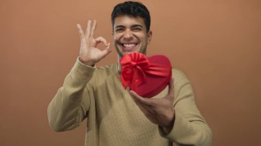 Adam yüreğini tutuyor ve stüdyoda tabelayı boyuyor çünkü genç görünen adam renkli kırmızı hediye geçmişine karşı..