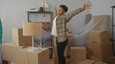 Genç adam, modern apartman odasındaki kutularla çevrili yeni evinde rahatlamış atmosferde yeni bir başlangıç önerisi sunuyor.