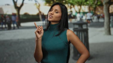 Sokaktaki genç İspanyol kadın çevresi insanlarla ve yeşilliklerle çevriliyken fikir jesti yapıyor.