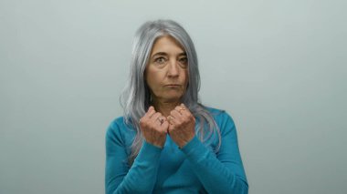 Beyaz arka planda mavi gömlekli son sınıf öğrencisi kadın. Yumruk duruşunu ve gücünü gösteriyor. Odaklanmış ifadesi sade bir ortama karşı.