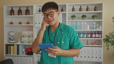 Tıbbi malzeme ve dosyalarla çevrili bir şekilde hastane odasında telefonla konuşan genç doktor profesyonel bir klinik ortamı sergiliyor..