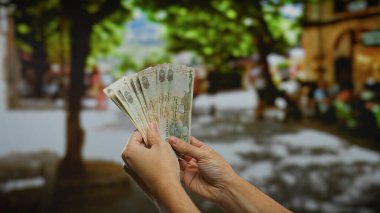 Kentsel bir sokak ortamında elinde kirli para tutan adam, hareketli bir şehir ortamında iş alışverişlerini ve finansal temaları vurguluyor..