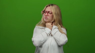 Yeşil bir arka plan üzerinde boynunu tutmaktan rahatsız olan bir kadın gözlük ve sağlık sorununu veya stresi tasvir eden beyaz bir gömlek giyiyor.