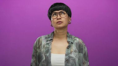 Genç Çinli bir kadın canlı mor bir arkaplan, gözlük ve desenli bir gömlek takıyor. Tecrit edilmiş bir ortamda duygu ve bireyselliği işaret ediyor.