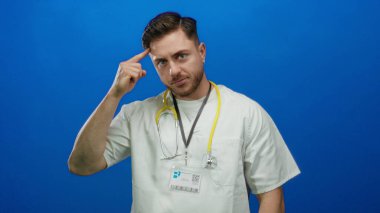 Kafasında sakal ve steteskop olan genç bir doktor canlı mavi arka plana karşı güvenli bir şekilde izole edilmiş, düşünceli ve tıbbi profesyonelliği iletiyor..