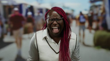 Pazar caddesinde neşeli bir şekilde gülen bir kadın. Etrafı güneşli şehir gününde insanlarla çevrili. Canlı bir atmosfer var..