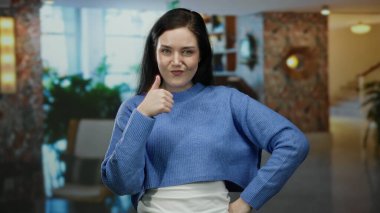 Zarif otel lobisinde elleri gösterişli bir kadın. Pozitif ve kendine güvenen bir duruş sergiliyor. Girişte parlak iç dekorasyonu olan mavi süveter giyiyor..