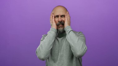 Gri kazaklı kel adam, elleri ile hareket eden, soyutlanmış mor arka plana karşı düşünceli görünüyor..