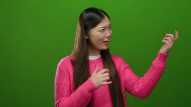 Gitar çalan kadın, canlı yeşil arka plana karşı pembe süveter giyerek güven içinde poz veriyor ve neşe ve yaratıcılığı yakalıyor.