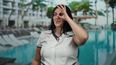 Tatil köyünde havuz başında dikilen bir kadın, dışarıda tropikal rahatlama ve rahatlama zeminine karşı kendine güveni tam bir jest yapıyor..