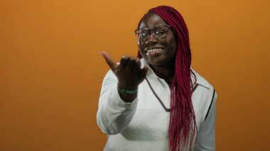 Turuncu bir duvara karşı neşeli bir hareketle gülümseyen kadın neşeli kırmızı örgülerini ve şık gözlüklerini gösteriyordu..