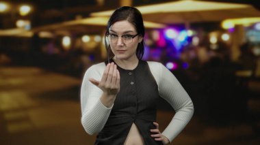 Gece canlı bir terasta gözlüklü gülümseyen bir kadın. Bulanık restoran ışıklarıyla sıcak bir sokak havası yaratıyor..