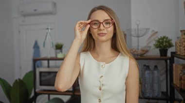 Modern ofis içlerindeki gözlükleri ayarlayan kadın, yaratıcı bir iş yeri olduğunu gösteren şık dekorlar ve kapalı mekanlarla çevrili profesyonel bir ortama güvendiğini gösteriyor..