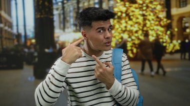 Genç adam, şehir sokaklarının ışıklarıyla dolu bir arka planda ilginç bir ifadeyi ve gece ortamında sıradan bir modayı vurguluyor..