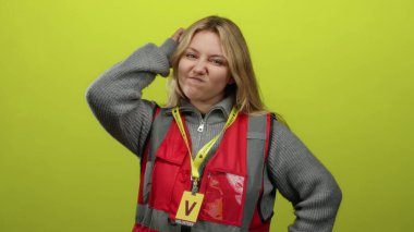 Kırmızı yelek giyen genç sarışın kadın mavi arka plan duvarına karşı duruyor, elleri kafasında duygularını gösteriyor..