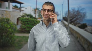 Güneşli bir sokakta, açık havada, okyanus kenarında konuşurken gülümseyen bir adam kıyı kentlerinde rahat bir yaşam tarzı ve iletişim sergiliyor..