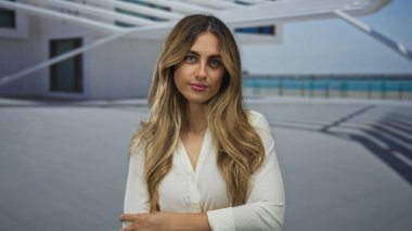 Kadın ön kolunu tutuyor ve terasta yan yana bakıyor; tefekkür yansıması.