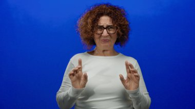 Mavi bir arka plana el kaldırarak tiksinen bir kadın basit bir ortamda net duygular sergiliyor..