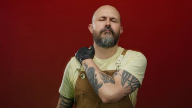 Kırmızı arka planda sakallı bir adam boynuna dokunuyor stüdyo ortamında izole bir şekilde acı içinde görünüyor..