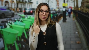 Dışarıda kutlayan genç bir kadın kalabalık bir caddede, bisikletlerle ve şehir hayatıyla çevrili, heyecan ve hareketlilik gösteren jestlerle..