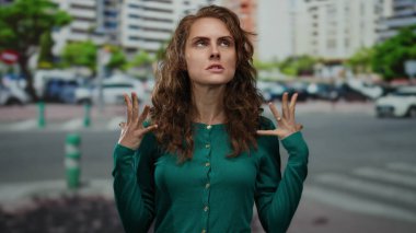 Şehir caddesinde arka planda binaları olan yeşil kazak giyen düşünceli ve düşünceli bir kadın..