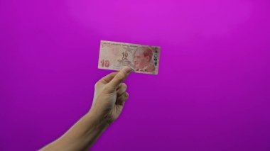 Canlı mor bir duvara karşı Türk lirası banknot tutan adam, izole bir para birimi gösteriyor, finans ve ekonomi kavramını vurguluyor..