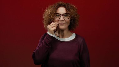 Esmer kadın, kültürel ifadelerini sergileyen canlı kırmızı duvara karşı sessizliğini gösteriyor..