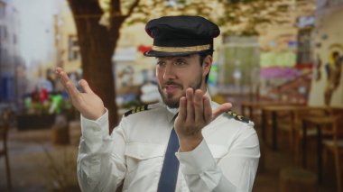 Sakallı ve pilot üniformalı genç adam restoranın terasında arka planı bulanık, rahatlamış bir kahve dükkanı atmosferi sergiliyor..