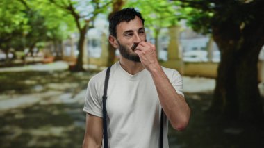 Sakallı İspanyol bir adam açık havada keyif ve haz sunan ağaçlarla çevrili yemyeşil bir parkta şef öpücüğü jesti yapıyor..