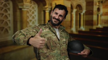 Askeri üniformalı ve sakallı bir adam katolik kilise ortamında, dekoratif mimari ile çevrili bir ortamda, güven duygusunu dile getiriyor..