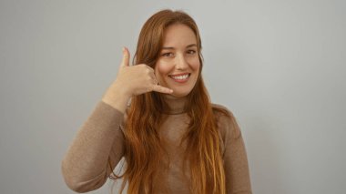 Gülümseyen bir kadın beyaz arka planda el hareketleriyle doğal güzelliğini ve günlük kıyafetlerini sergileyerek sakin ve dostça bir yüz ifadesi yakalıyor..