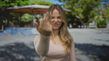 Uçan sarı saçlı bir kadın güneş ışığı altında orta parmağını hareket ettirir. İsyan isyanının öfkesi azimlidir..