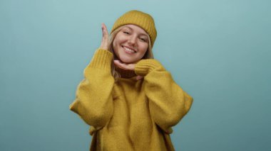 Sade sarı bir kazak ve uyumlu bir bereyle gülümseyen bir kadın, saf mavi bir arka planda sıcaklığı ve mutluluğu izole bir duvarda yakalıyor..