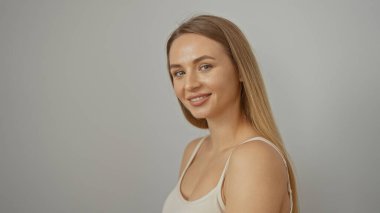 Beyaz bir arka plana güvenle gülümseyen bir kadın uzun sarı saçlı ve sıradan kıyafetli güzelliğini sergiliyor, gençlik zarafetini ve sadeliğini sunuyor..