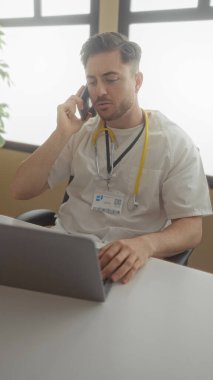 Hastane odasında sakallı genç bir adam bilgisayarla ve steteskopla konuşuyor. İçerideki bir tıp fakültesinde doktorluk mesleğini gösteriyor..