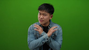 Kot ceketli genç adam, yeşil arka plana karşı olumsuz duygular besliyordu. Elleri çapraz olsun ya da olmasın, bir anlaşmazlık vardı..