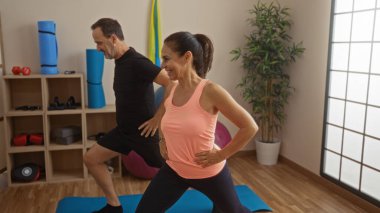 Orta yaşlı İspanyol çift spor salonunda ekipmanlarıyla birlikte egzersiz yapıyor, kapalı bir spor merkezinde sevgi ve sağlığını yansıtıyor..