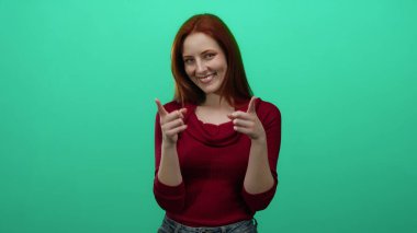 Neşeli bir gülümsemeyle kamerayı gösteren bir kadın, kırmızı saçlı, kırmızı bir kazak giyen, parlak yeşil duvarlı bir arka plan.