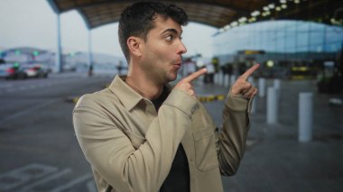 Adam, terminalde genç İspanyol havaalanı yolcusunun yanında erkek gözlemci olarak heyecanlı görünen işaretlere işaret ederken elini kaldırıyor..