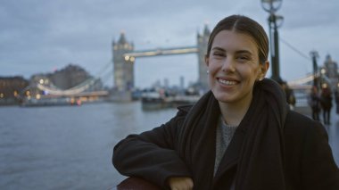 Londra 'da ünlü köprü geçmişi olan nehir kenarında gülümseyen bir kadın alacakaranlıkta İspanyol titreşimleriyle şehir modasını sergiliyor, canlı şehir ruhunu yakalıyor..